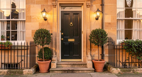 A Georgian townhouse guest house front door with a brass knocker and potted bay trees on a honey sandstone street in Alnwick.