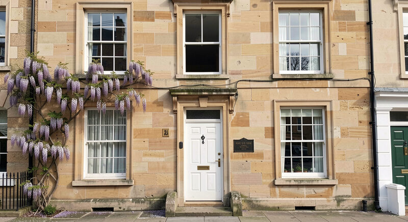 A Georgian sandstone townhouse facade with a blocked first floor window and a small fire insurance plaque fixed above the front door.